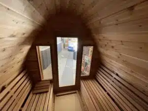 L'intérieur d'un sauna en bois avec deux bancs se faisant face le long des parois latérales. Le mur du fond comporte trois fenêtres verticales, laissant entrer la lumière naturelle pour éclairer le sauna. Le bois crée une atmosphère chaleureuse et invitante.