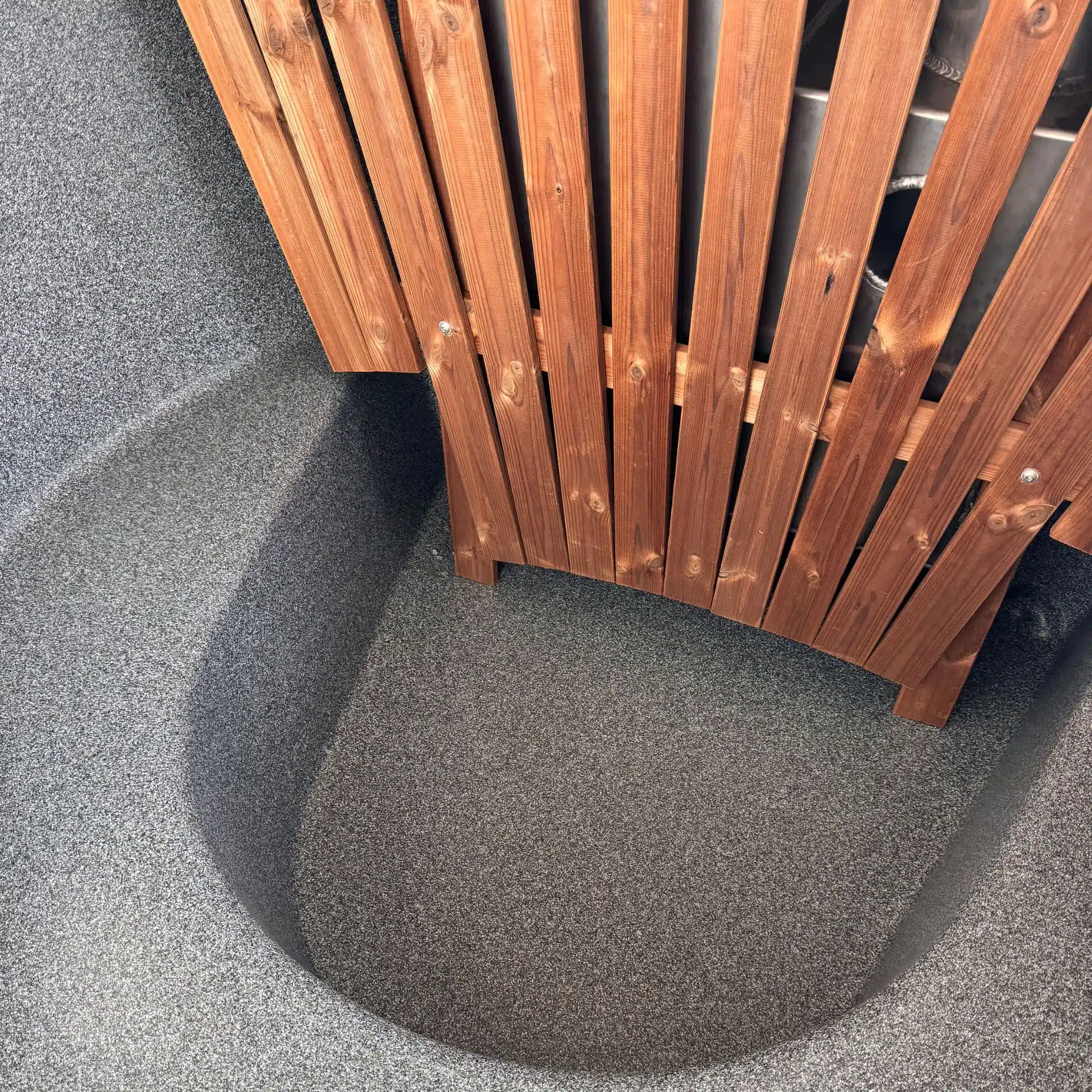 Un gros plan montre un panneau en lattes de bois recouvrant partiellement le dessus d'un bassin gris, texturé et incurvé, faisant partie du Bain nordique en bois.