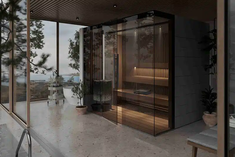 Sauna moderne aux parois de verre avec intérieur en bois et cabine Hammam Tylö à l'intérieur d'une maison élégante ; de grandes fenêtres révèlent des vues panoramiques sur l'extérieur des arbres et de l'eau, tandis que les plantes en pot ajoutent une touche de fraîcheur à l'espace serein.
