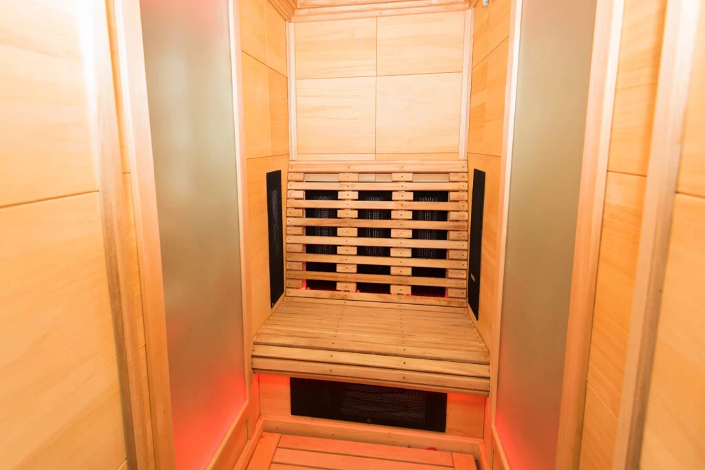 Un sauna infrarouge en bois, équipé d'un banc, de lambris en bois clair et d'un éclairage rouge tamisé sous la zone des sièges. Le sauna dégage une impression de propreté et de modernité.