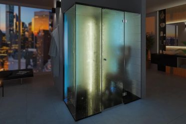 Une salle de bain moderne et faiblement éclairée avec un grand espace douche vitré rappelant un hammam, éclairé de l'intérieur et offrant une vue sur les toits de la ville à travers une large fenêtre. La pièce dispose également d'un lavabo élégant avec un miroir et une décoration de plantes vertes.